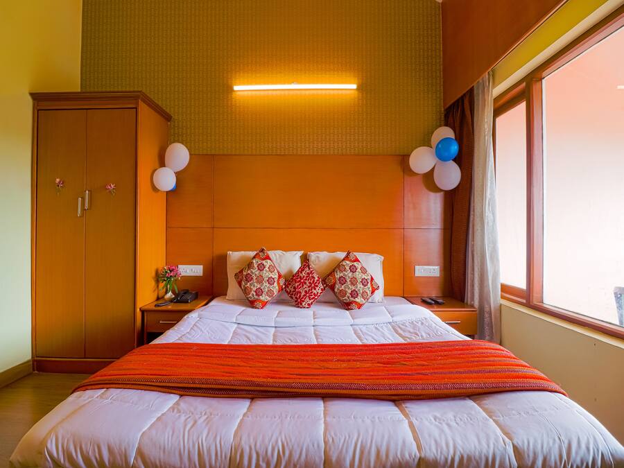 A hotel room with a large bed, a wooden wardrobe, a nightstand with a phone, and a window with a view.