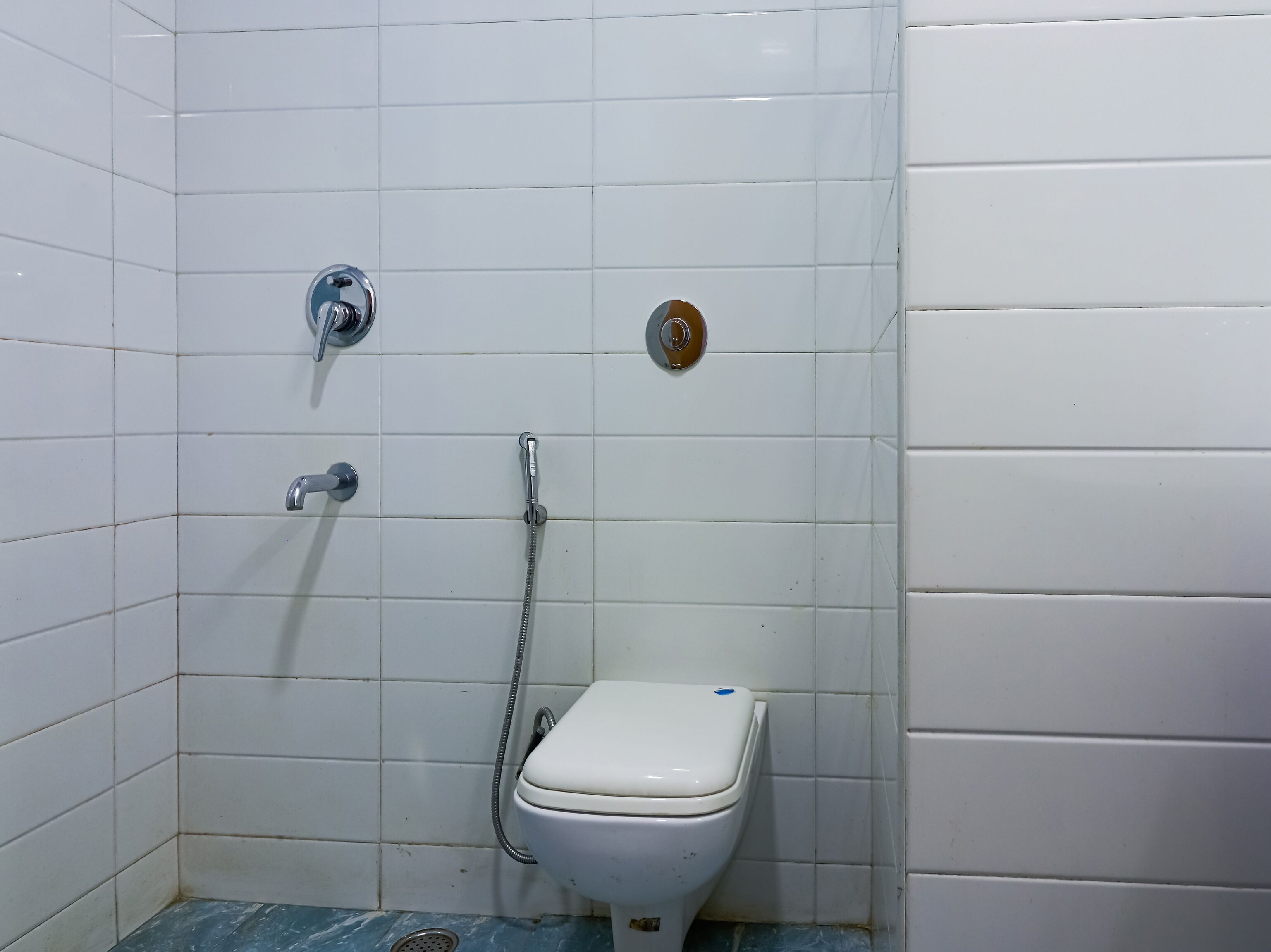 Ein kleines, sauberes Badezimmer mit weißen Fliesen, einer Toilette, einer Duschbrause und einem Wasserhahn.
