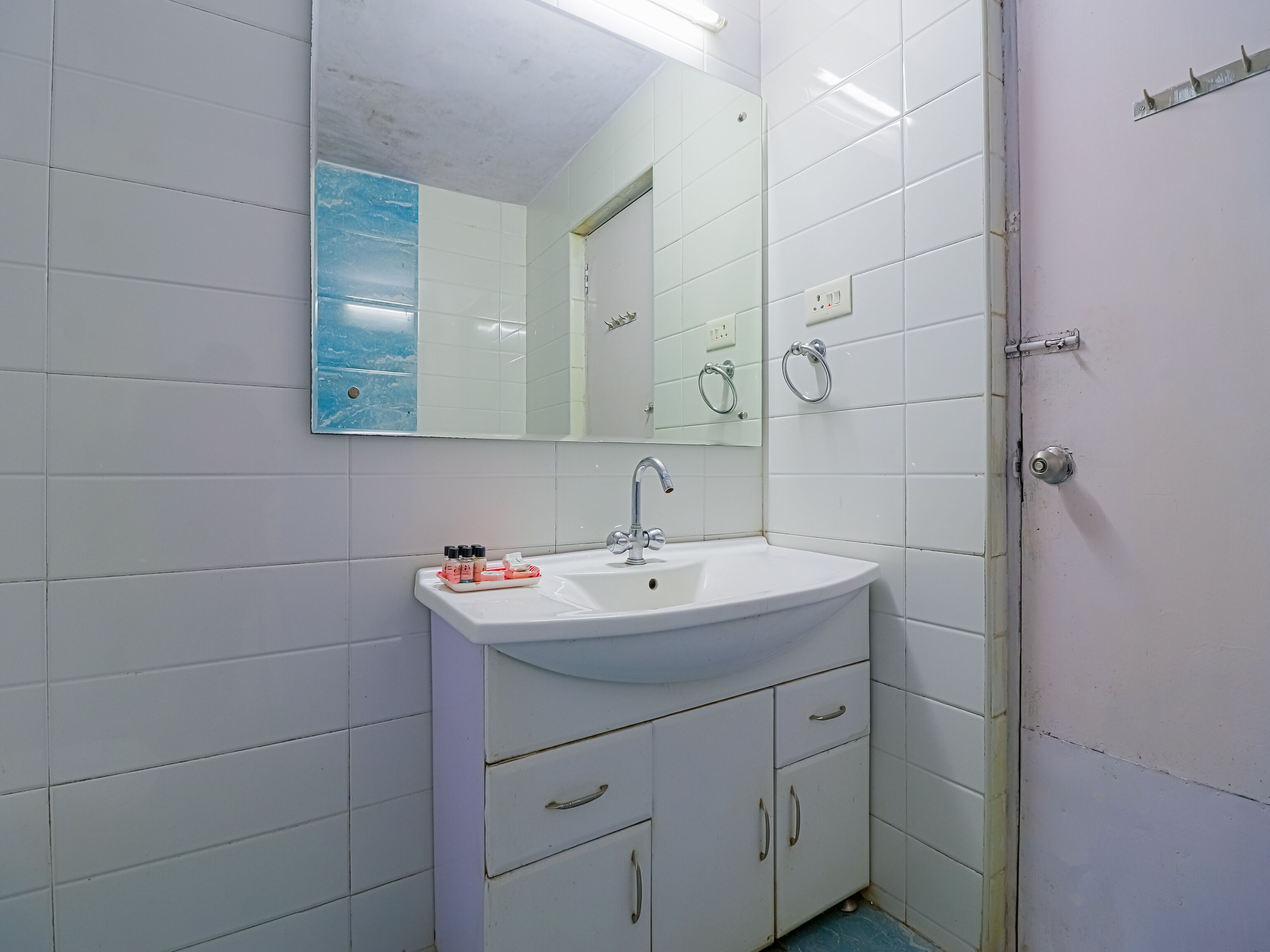 A bathroom with white tiles, a sink, a mirror, and a door.