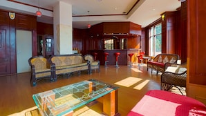 A spacious living area with a glass-top coffee table, wicker furniture, and a kitchen in the background.
