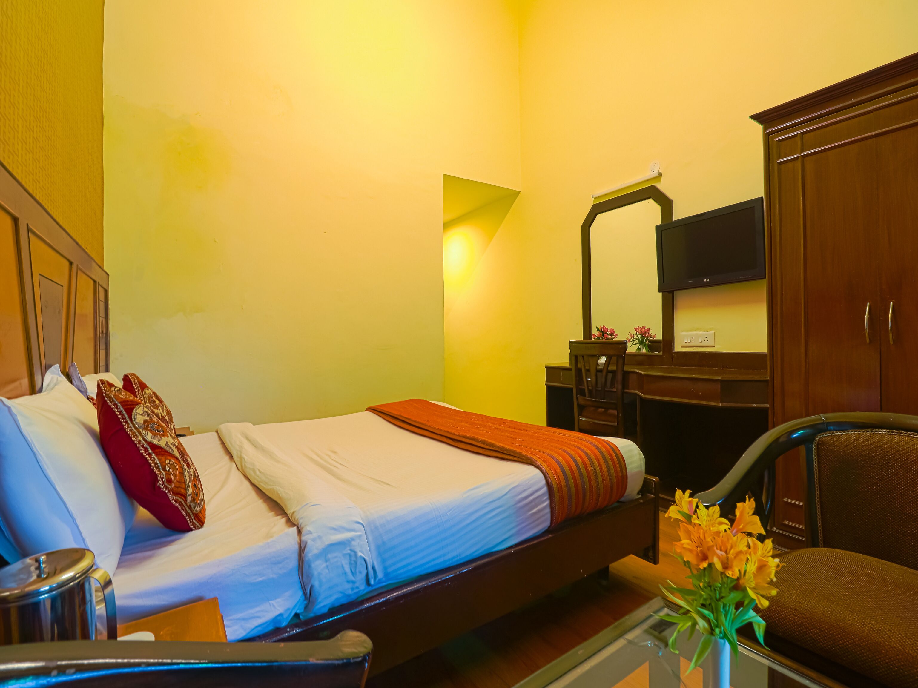 A hotel room with a bed, a desk, a chair, a TV, and a vase with flowers.