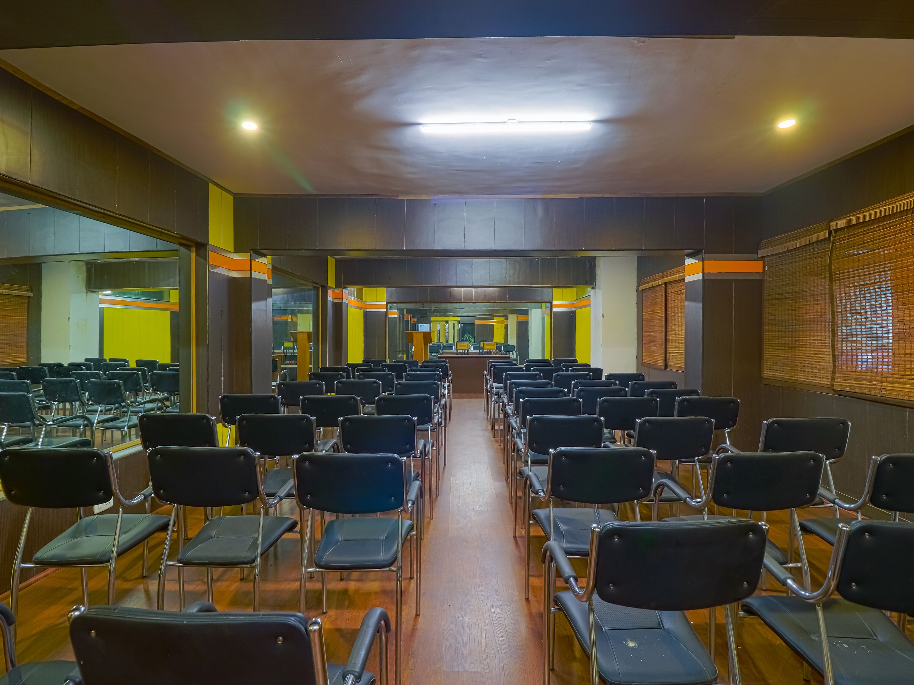 A conference room with rows of chairs, a wooden floor, and a ceiling with recessed lighting.