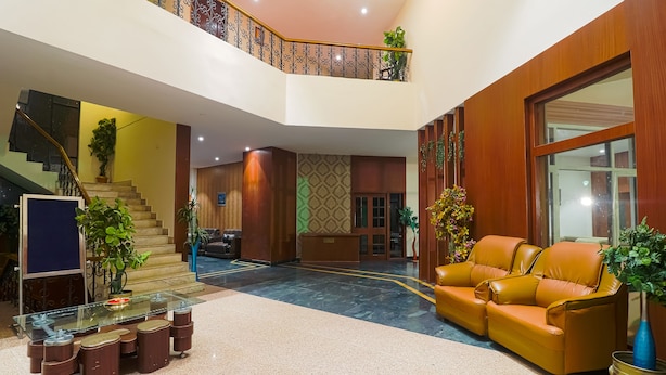 A hotel lobby with a staircase, a reception desk, a seating area with a sofa, and a glass-top table with stools.