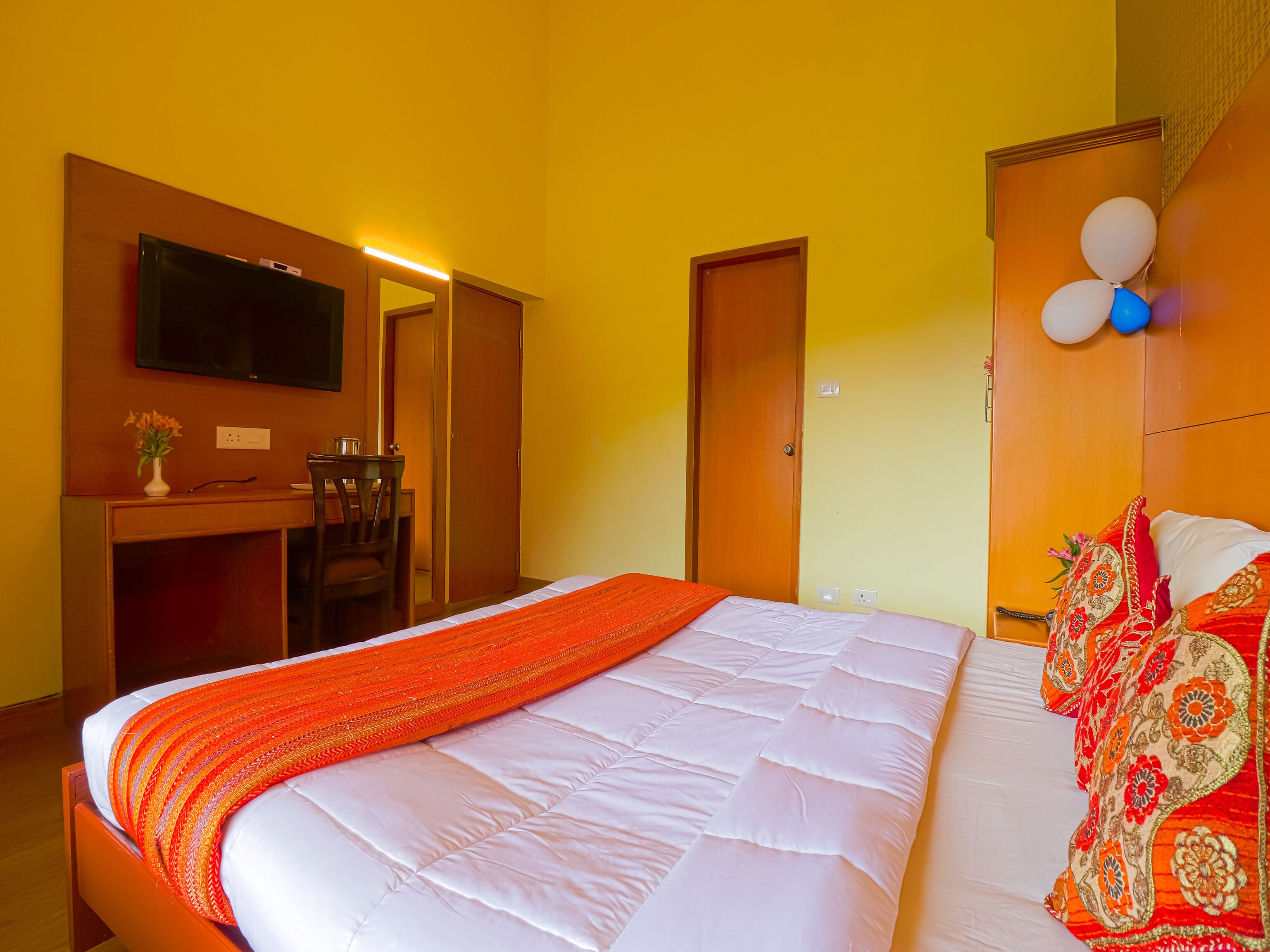 A hotel room with a bed, a desk with a chair, a television, and a door.