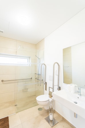 A modern bathroom with a glass shower enclosure, a white toilet, and a large sink with a mirror.