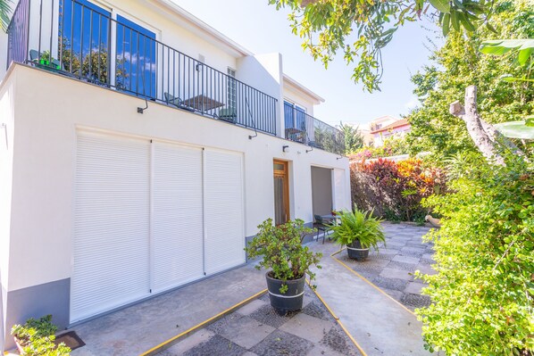 A modern two-story building with a balcony, a garage, and potted plants.