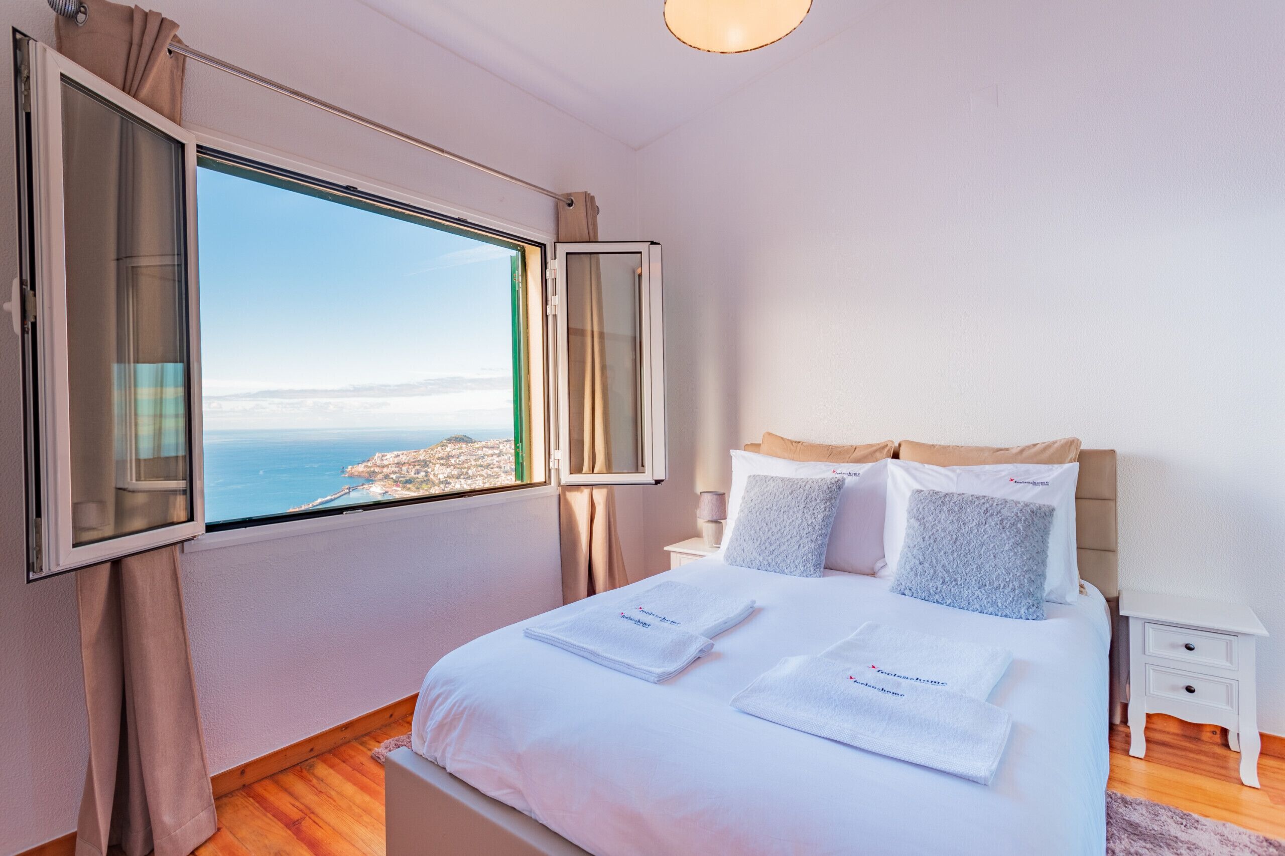 A hotel room with a large window, a bed with white linens, and a nightstand.
