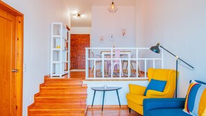 A living room with a wooden staircase, a yellow armchair, a blue sofa, a small round table, and a white bookshelf. - FLH Funchal Ocean View with Pool (Funchal)