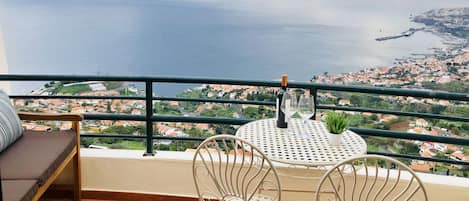 Ein Balkon mit Tisch und Stühlen mit Blick auf eine Küstenstadt und das Meer.