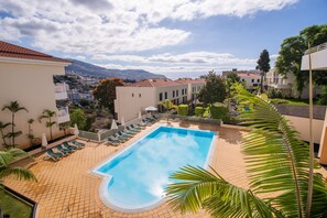 A swimming pool with lounge chairs, surrounded by buildings and a view of a distant town and mountains. - FLH Funchal Modern Apartment with Pool (Funchal)