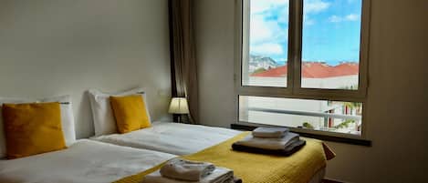 Une chambre d’hôtel avec deux lits, une fenêtre donnant sur des immeubles, une lampe et des serviettes sur les lits.