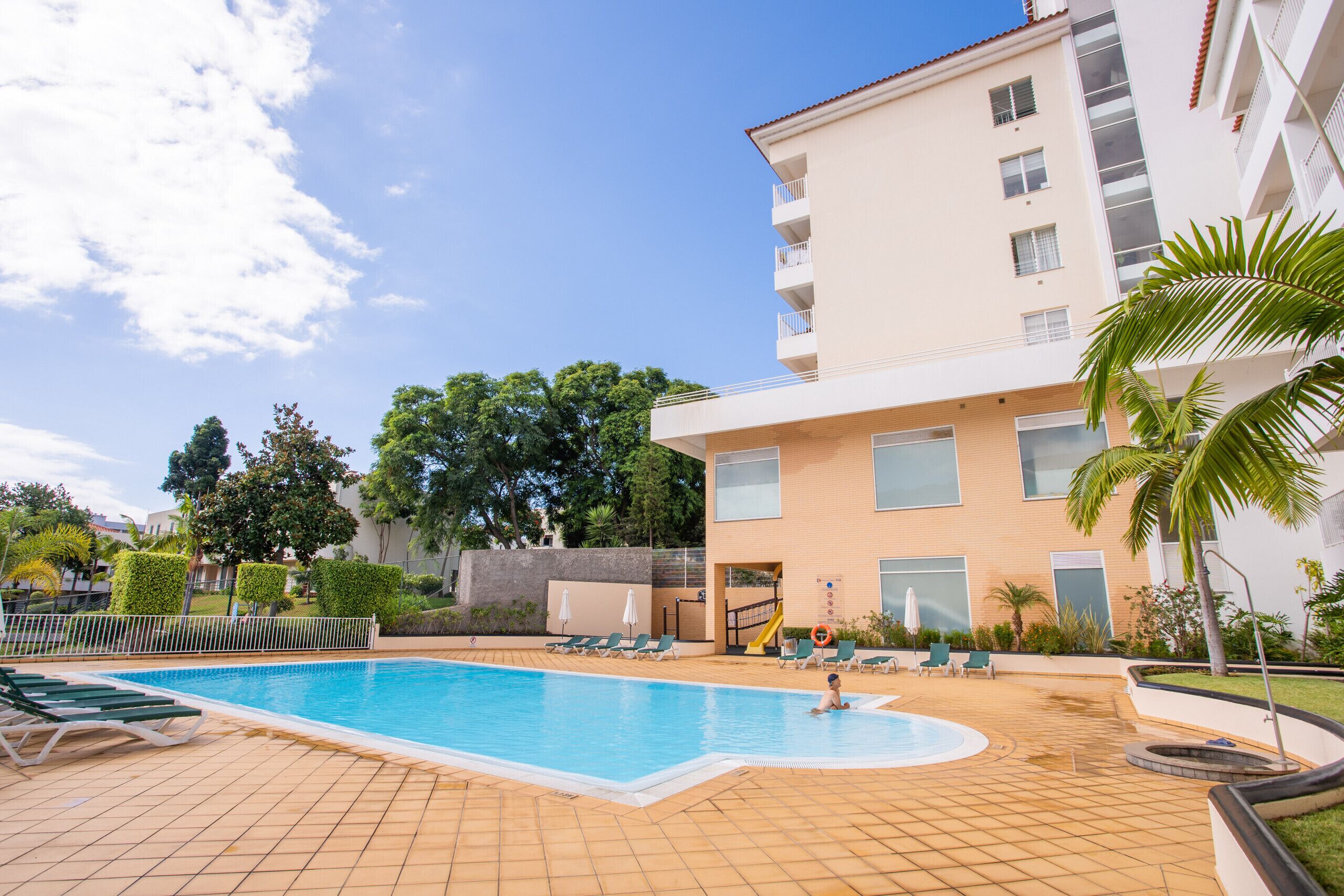 A swimming pool with lounge chairs, a slide, and a building with balconies.