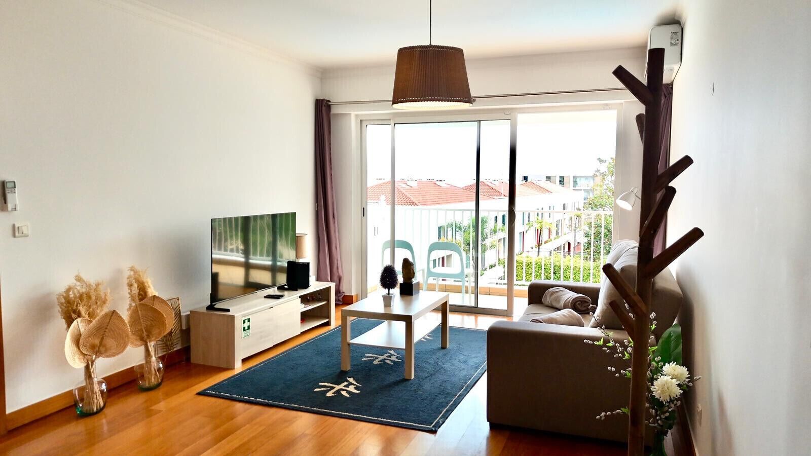 Een moderne woonkamer met een televisie, bank, eettafel en een balkon met uitzicht op gebouwen.