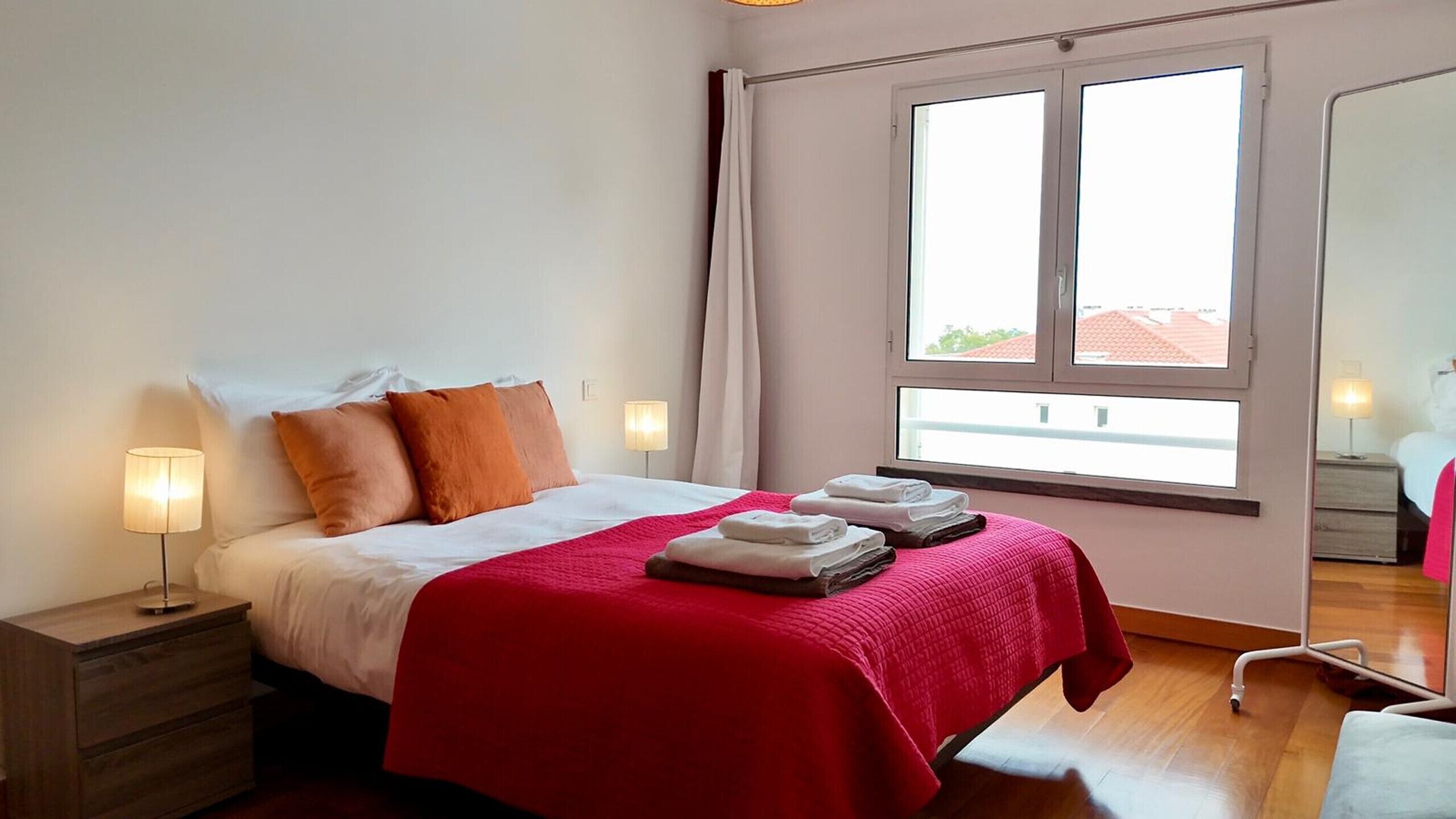 Una habitación de hotel con cama, lámparas de noche, ventana con cortinas y una silla.