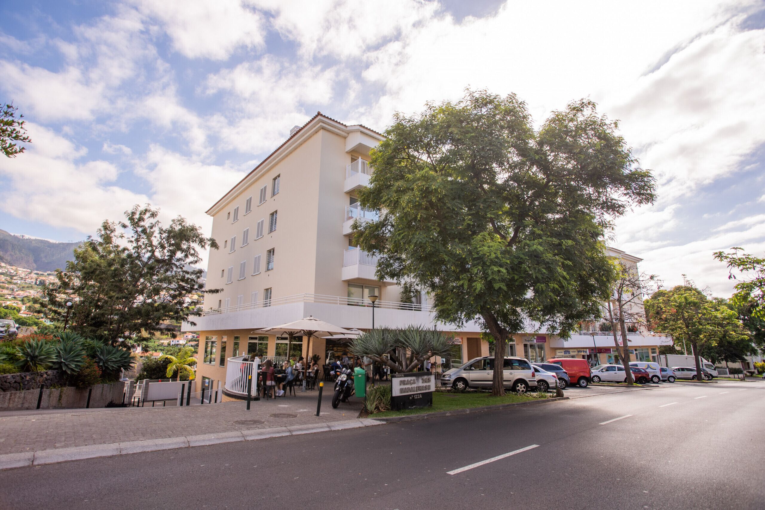 Un hôtel à plusieurs étages doté d’un balcon au deuxième étage, d’un parking avec plusieurs voitures et offrant une vue sur les environs.