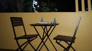 An outdoor balcony with two black folding chairs and a small table, a yellow wall, and a view of the night sky and distant lights. - Close to Carnival &  POS activities! Secure 1 bdr apt, mins from Port of Spain (St Anns)