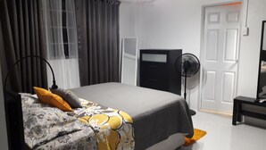 A bedroom with a bed, a bedside table, a lamp, a fan, and a wardrobe. - Close to Carnival &  POS activities! Secure 1 bdr apt, mins from Port of Spain (St Anns)
