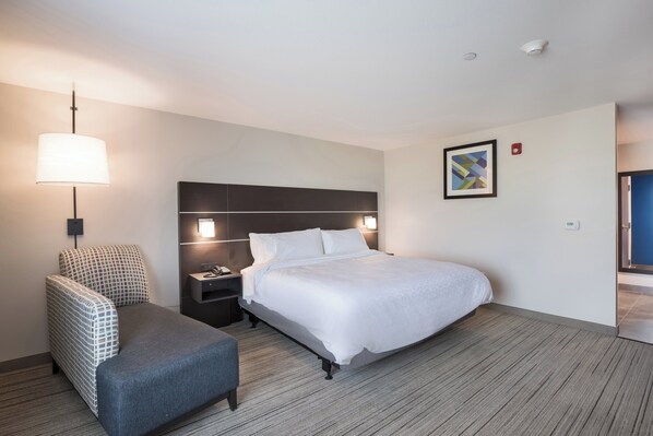 A hotel room with a bed, a chair, a nightstand, a lamp, and a painting on the wall.