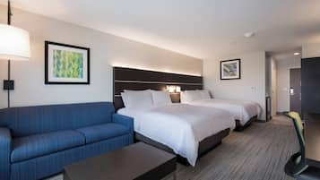 A hotel room with a bed, a sofa, a desk, and two framed artworks on the walls.