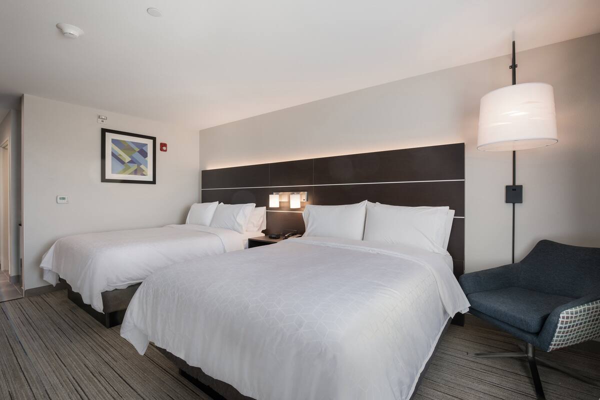 Une chambre d’hôtel avec deux lits, une table de chevet, une lampe, une chaise et un tableau encadré au mur.