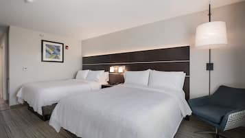A hotel room with two beds, a nightstand, a lamp, a chair, and a framed picture on the wall.