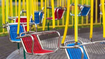 A row of empty swing seats with metal frames and woven seats in red, blue, and yellow colors.