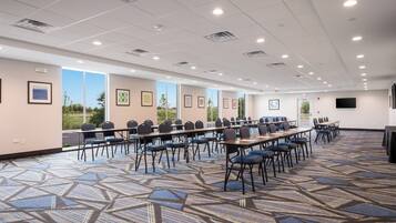 A conference room with multiple tables and chairs, large windows, and a patterned carpet.