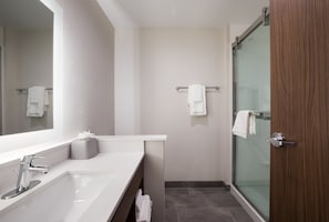 Een moderne badkamer met een grote spiegel, een wit wastafelmeubel, een douchecabine van glas en een houten deur.