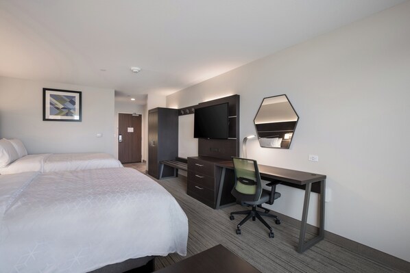 Quarto de hotel com uma cama, escrivaninha, cadeira, televisão e espelho.