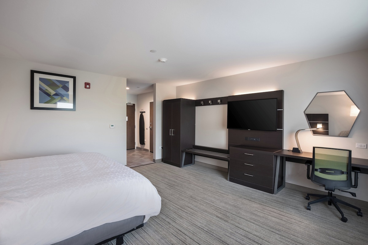 Hotelkamer met een bed, bureau, stoel, kledingkast, spiegel en een lijst aan de muur.