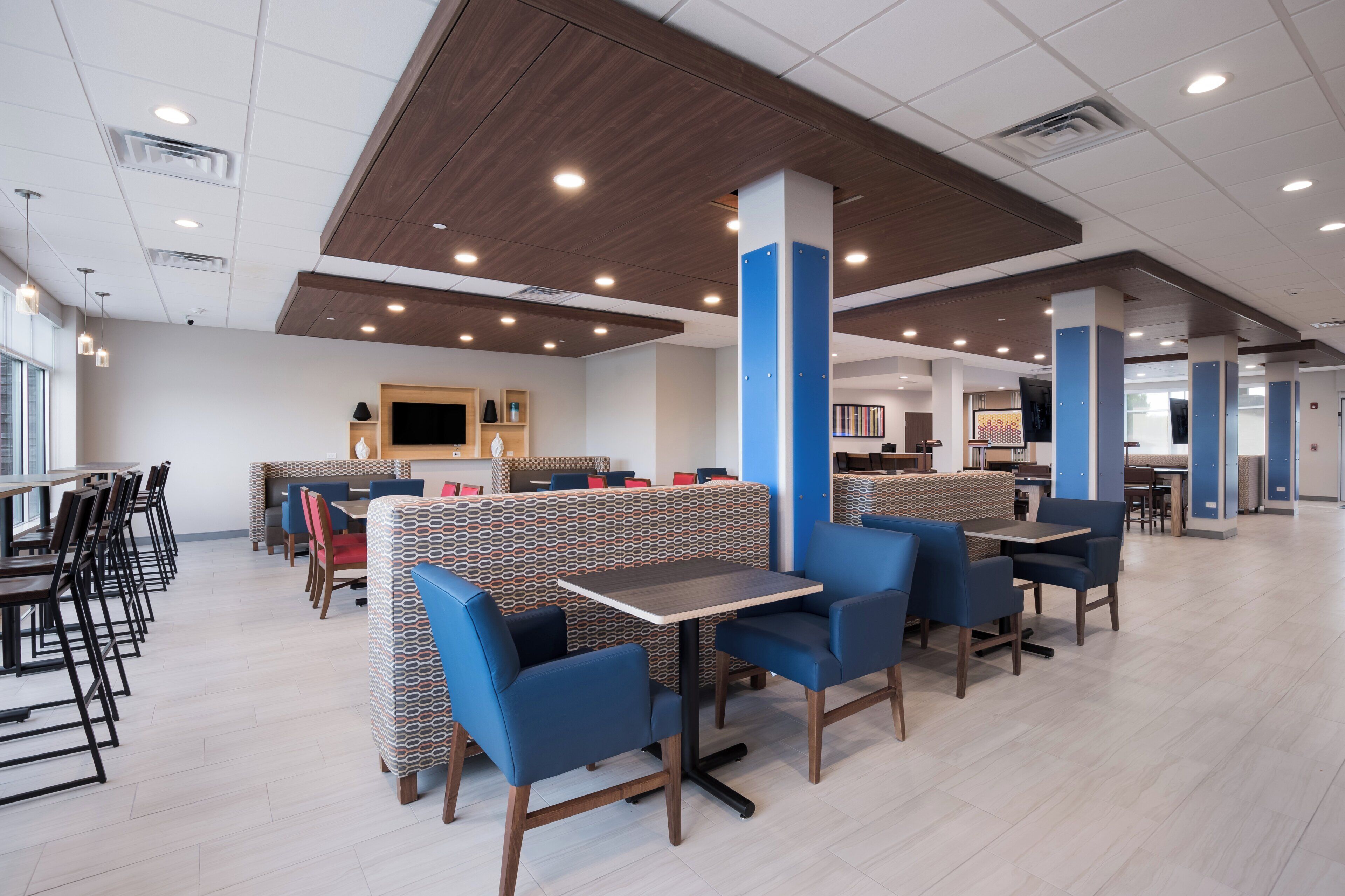 A modern restaurant with booths and tables, wooden ceiling, and recessed lighting.