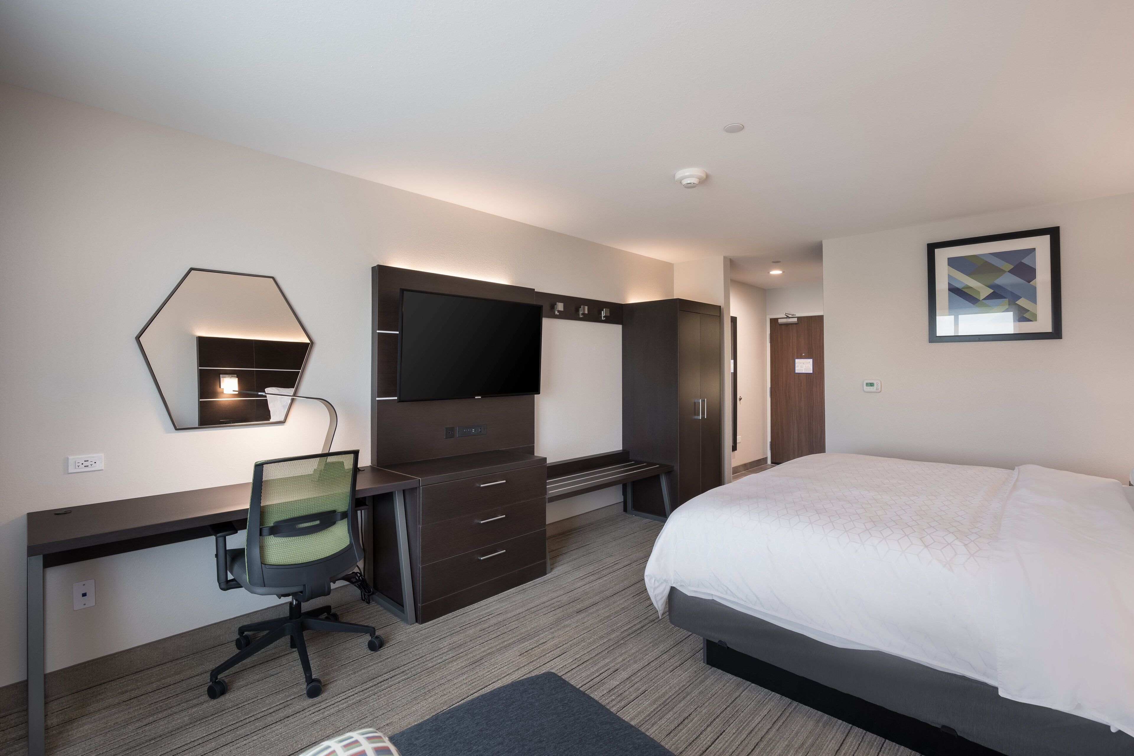 A hotel room with a bed, a desk with a chair, a TV, and a wardrobe.