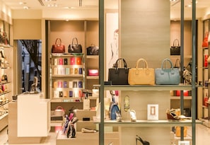 Een luxe handtaswinkel met rijen handtassen en een etalage met schoenen.