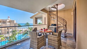 A balcony with wicker furniture, a spiral staircase, and a view of a swimming pool and buildings. - Playa del Carmen Beachfront Condo w/ Pool Access! (Playa Del Carmen)
