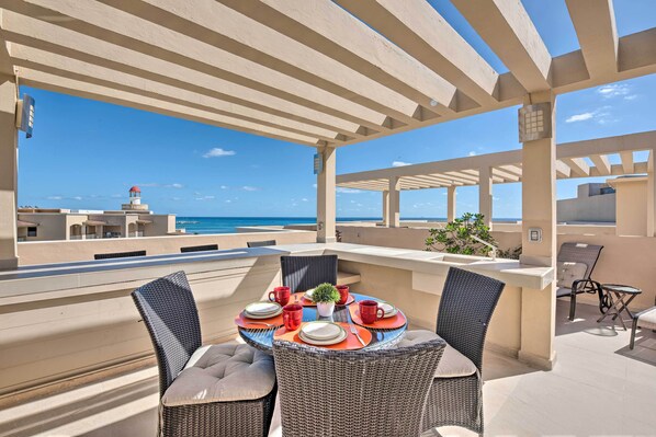 Une terrasse extérieure avec une table dressée pour le dîner, offrant une vue sur une plage et un phare.
