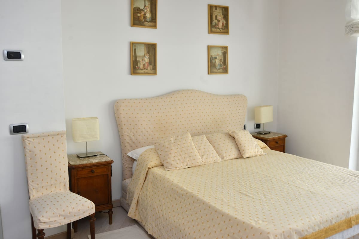 Ein Schlafzimmer mit einem Bett, einem Sessel, zwei Nachttischen und vier an der Wand befestigten Bildern.