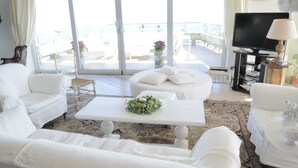 A white-themed living room with a large window, a flat-screen TV, and a small table with a floral centerpiece. - Maison Blanche Luxury B&B Taormina (Taormina)