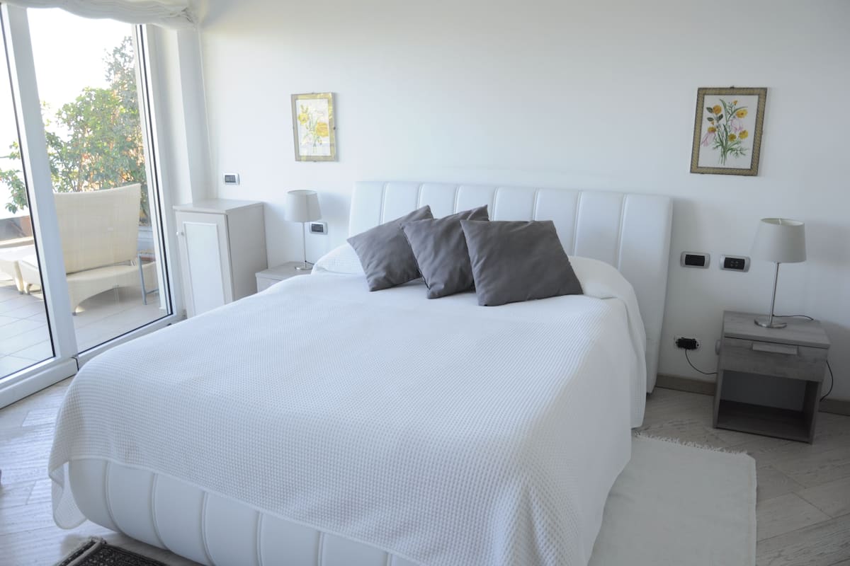 Ein Schlafzimmer mit einem großen Bett, zwei Nachttischen, einem Fenster und Blick ins Freie.