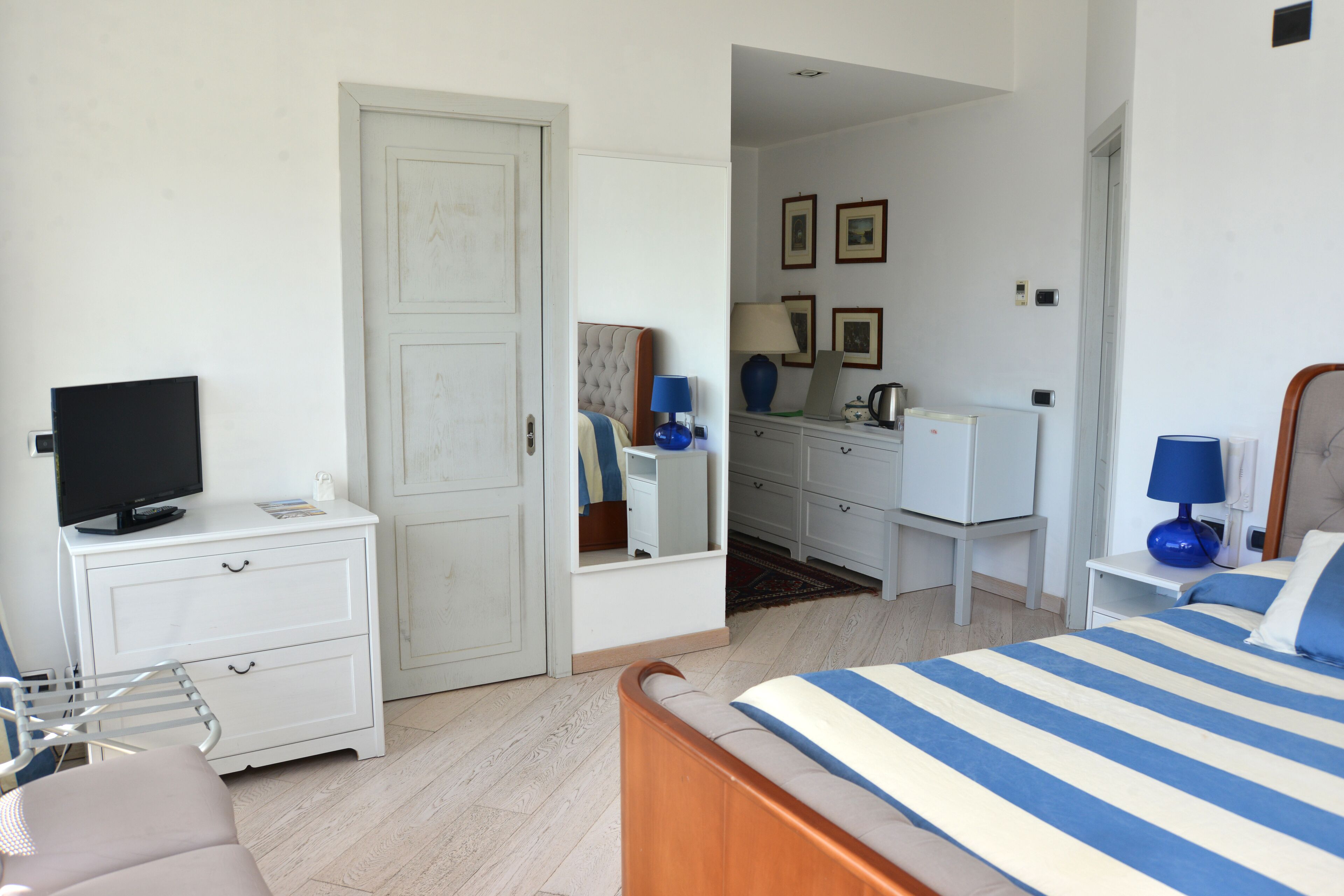 A bedroom with a bed, a TV on a nightstand, a dresser, and a mirror.