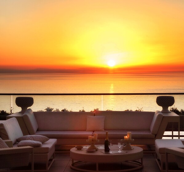 A sunset view from a balcony with a sofa, chairs, and a table set for dining. - Maison Blanche Luxury B&B Taormina (Taormina)