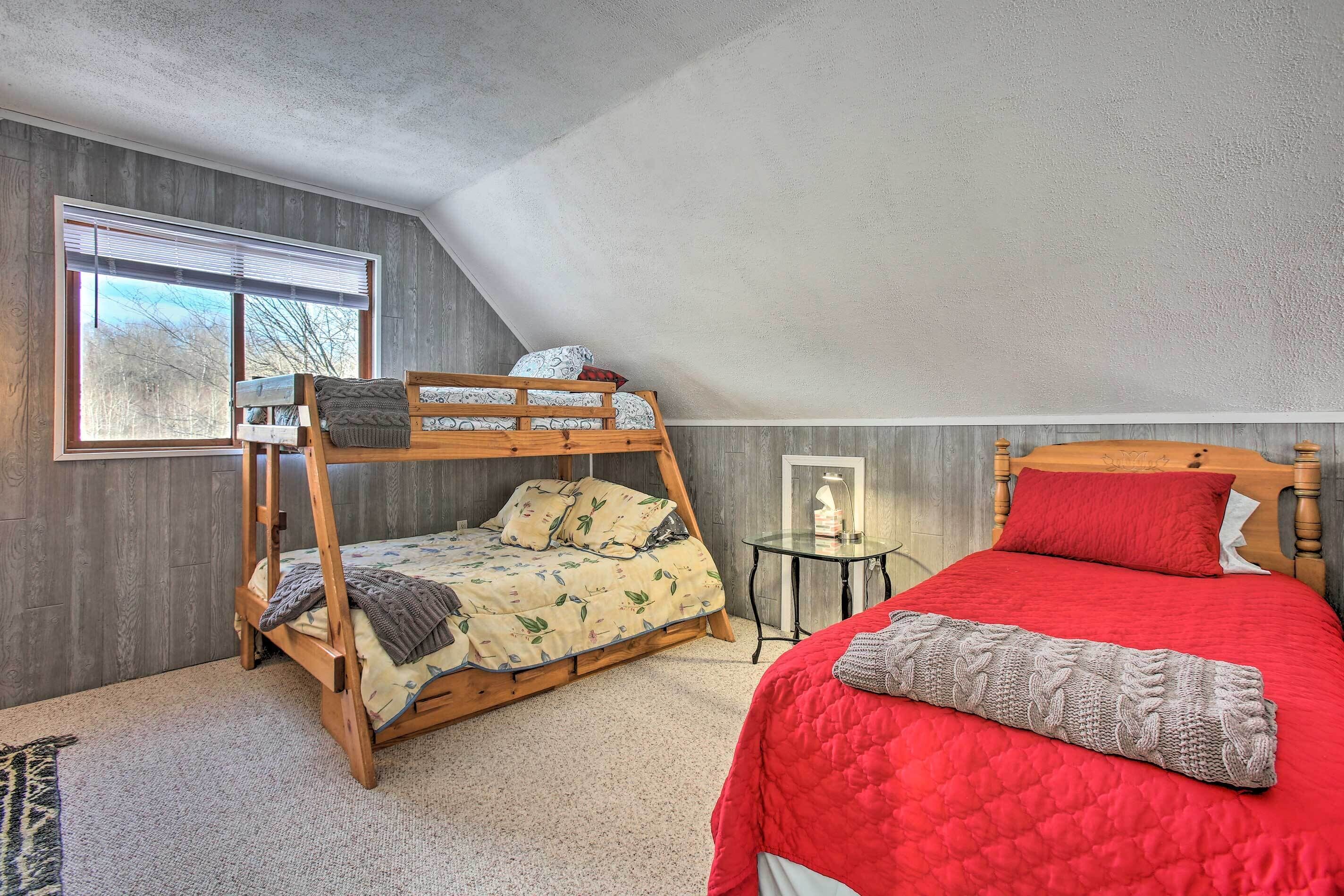 Ein Schlafzimmer mit einem Etagenbett, einem Einzelbett, einem kleinen Tisch und einem Fenster mit Jalousien.