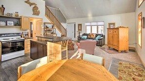 A spacious living area with a kitchen, dining table, and a staircase leading to an upper level. - Lakes of the North Home on Snowmobile & ATV Trail! (Mancelona)