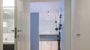 A hallway with wooden flooring leading to a kitchen area with white cabinets and a blue accent wall. - StayPlus Apt In Trendy Area WBalcony (Oslo)
