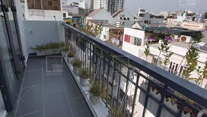 A balcony with a view of surrounding buildings, a railing, and potted plants.