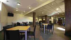 A spacious indoor area with multiple tables and chairs, a counter, and a television mounted on the wall. - Alberg Les Estades (Rialp)