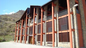 A multi-story building with a stone facade and red structural supports. - Alberg Les Estades (Rialp)
