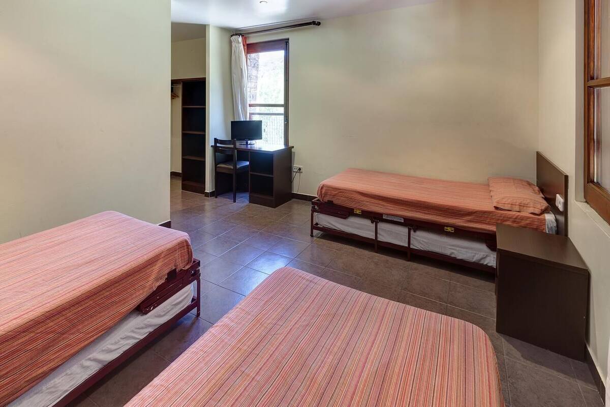A dormitory room with two single beds, a desk with a chair, and a television.