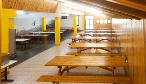 A cafeteria with wooden tables and chairs, a tiled floor, and a mural on the wall. - Alberg Les Estades (Rialp)