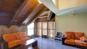 A spacious living room with wooden beams, two orange sofas, a coffee table, and a large window with curtains. - Alberg Les Estades (Rialp)