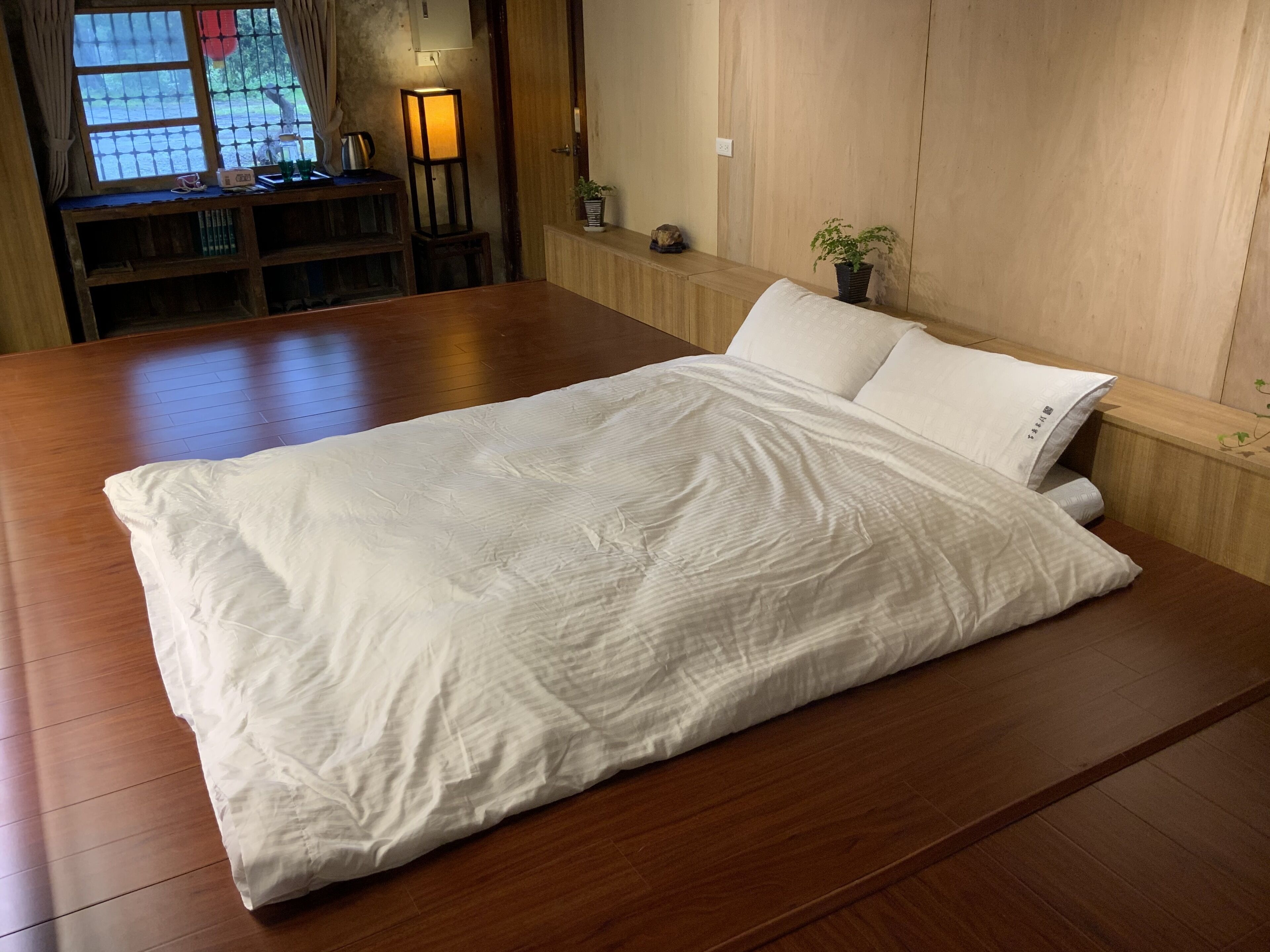 A neatly made bed with white bedding in a room with wooden flooring and a wooden headboard.